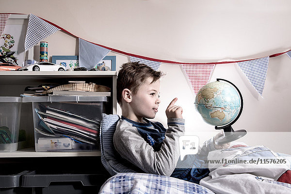 Junge sitzt aufrecht im Bett und zeigt auf Globus