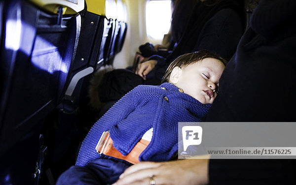 Kleiner Junge schläft auf dem Knie der Mutter im Flugzeug