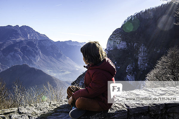 Junge sitzt auf einer Mauer und schaut auf die Berglandschaft  Italien