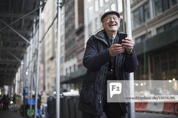 Mann lehnt an Laternenpfahl und hält Smartphone lachend  Manhattan  New York  USA