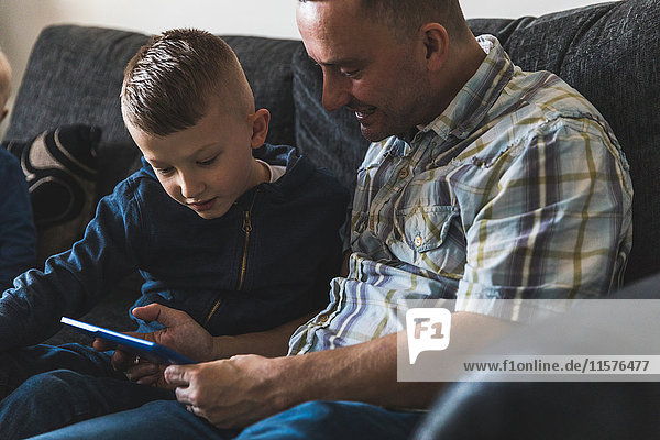 Father and son sitting on sofa looking at digital tablet