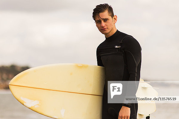 Porträt eines jungen Mannes  der ein Surfbrett hält