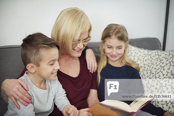 Großmutter und Enkelkinder lesen Buch auf Sofa