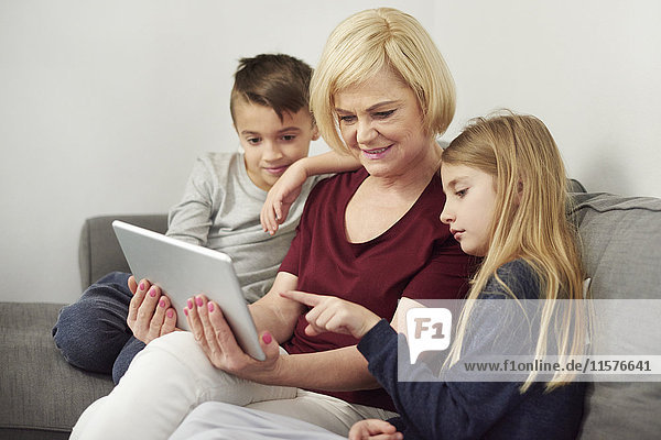 Großmutter und Enkelkinder mit digitalem Tablett auf dem Sofa