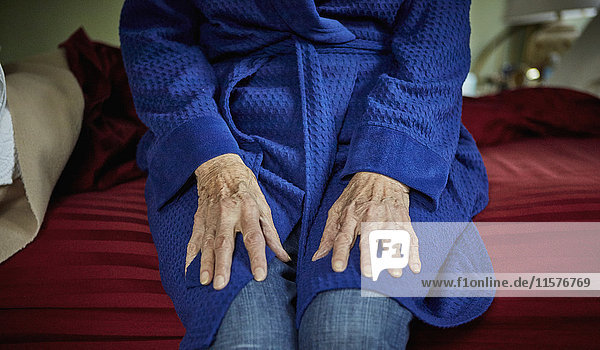 Ältere Frau auf Bettkante sitzend  Mittelteil