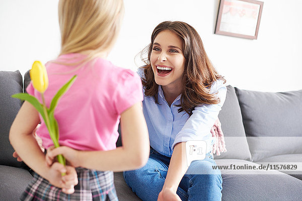 Mädchen versteckt Tulpengeschenk für Mutter auf Sofa