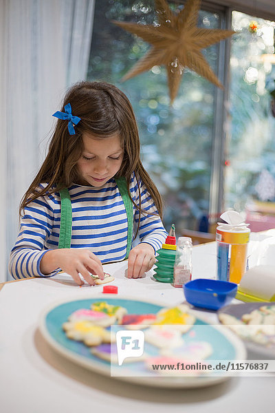 Mädchen schmückt Weihnachtsplätzchen für Teller auf der Küchentheke