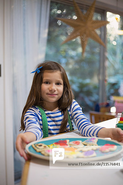 Stolzes Mädchen hält Teller mit dekorierten Weihnachtsplätzchen an der Küchentheke