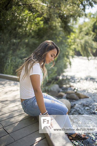 Teenager-Mädchen sitzt auf Fußgängerbrücke und starrt auf Fluss