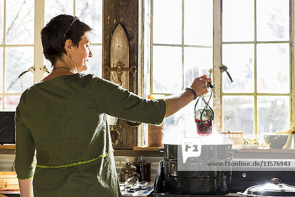 Rückansicht einer Frau  die ein Einmachglas mit Rote-Bete-Konserven aus einem dampfenden Kochtopf entfernt