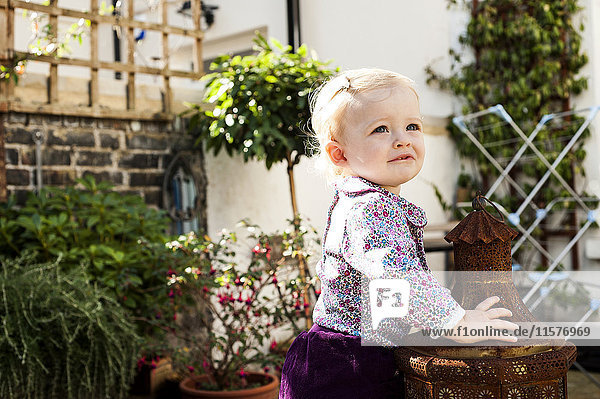 Kleines Mädchen stehend und lehnend an der Gartenlaterne