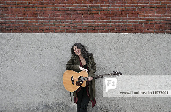 Porträt einer jungen Frau mit an die Wand gelehnter Akustikgitarre
