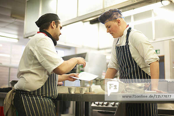 Chef lecturer explaining recipe to teenage catering student in college kitchen