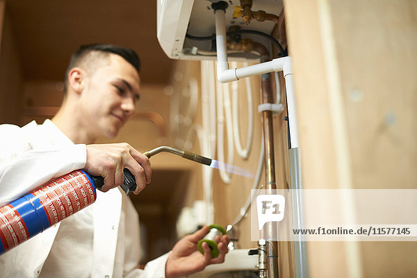 Junger männlicher Klempnerlehrling benutzt Blasbrenner an Rohrleitungen in einer College-Werkstatt