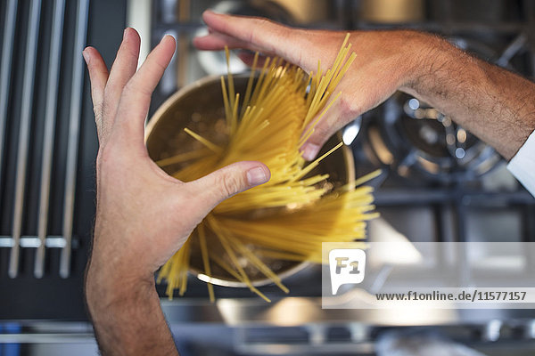 Koch  der Spaghetti in einem Kochtopf auf den Herd stellt  Nahaufnahme  Draufsicht