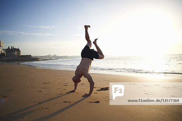 Erwachsener Mann macht Handstand am sonnenbeschienenen Strand  Cascais  Portugal