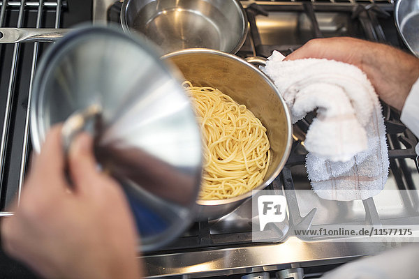 Chefkoch hebt Deckel auf Spaghetti-Pfanne auf dem Herd,  Ansicht von oben