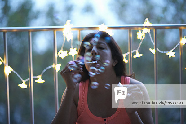Reife Frau bläst in der Abenddämmerung Blasen durch beleuchtete dekorative Lichter