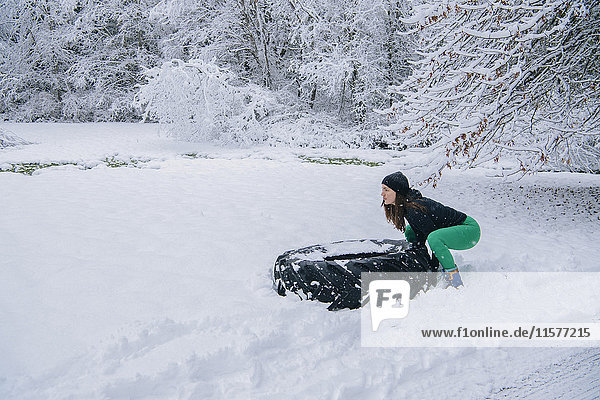 Woman trying to lift large tire in snow