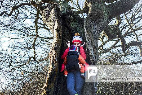 Frau in hohlem Baum  ein junges Baby im Tragetuch tragend