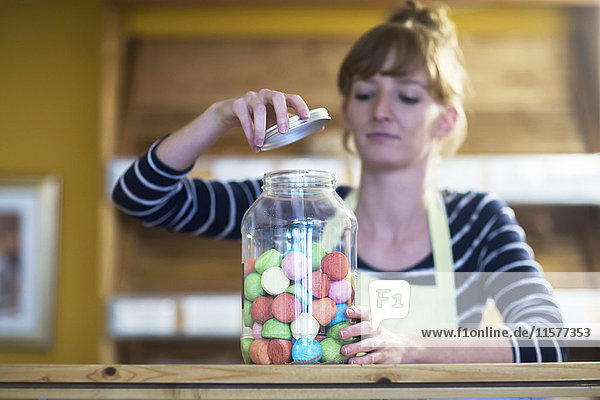 Junge Frau im Lebensmittelgeschäft  öffnet Glas mit Süßigkeiten