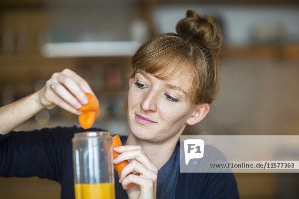 Young woman making smoothie with fresh carrot