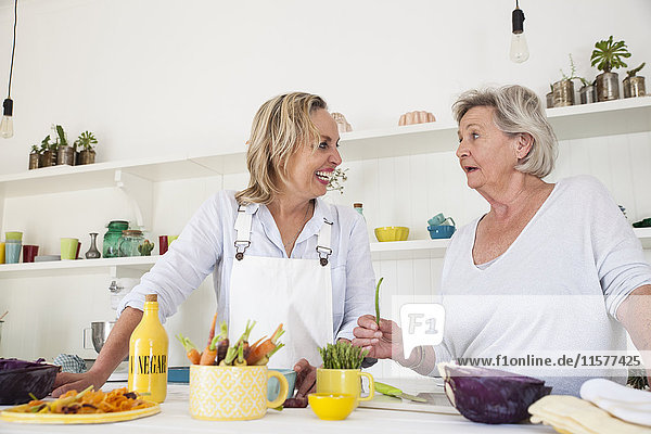Ältere Frau und Tochter unterhalten sich beim Zubereiten von Gemüse am Küchentisch