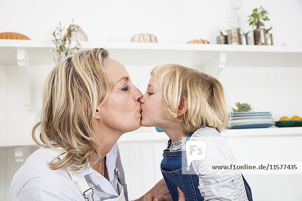 Girl kissing mother in kitchen