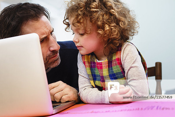 Mädchen blickt auf Vaters Laptop am Tisch