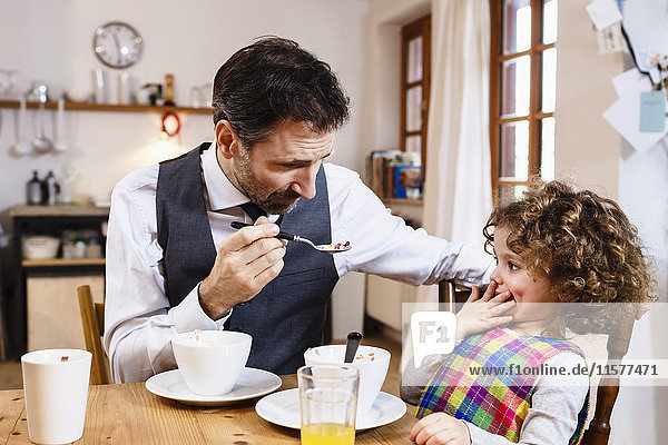 Man feeding daughter cereal with hand over mouth in kitchen
