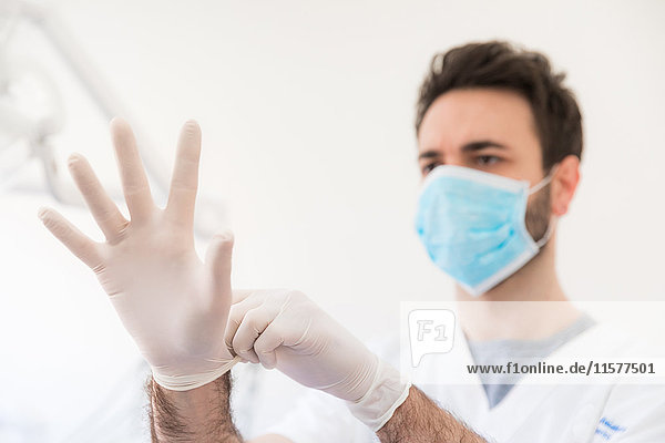 Männlicher Zahnarzt zieht Nitril-Handschuhe an