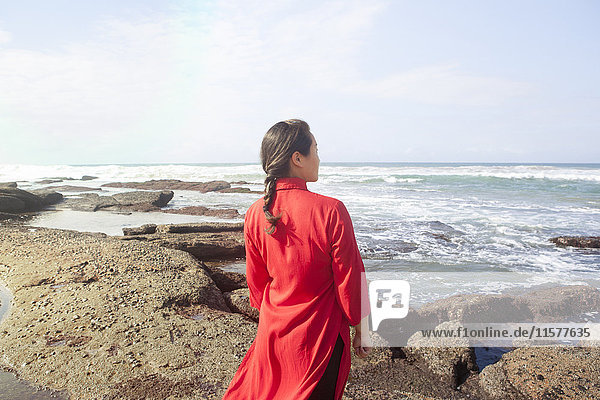 Frau in rotem Kleid  auf Felsen stehend  auf das Meer blickend  Südafrika