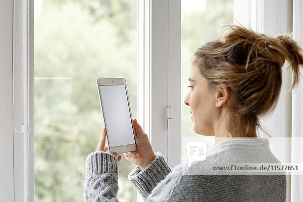 Woman at home  standing beside window  using digital tablet
