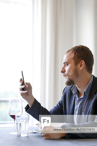 Mann sitzt am Esstisch und benutzt ein Smartphone