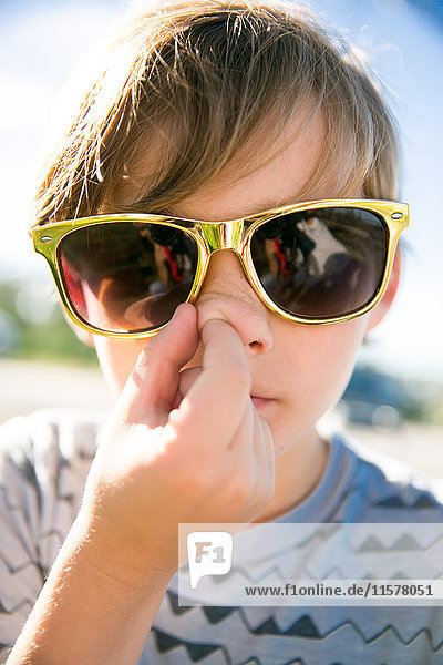 Portrait of boy in golden sunglasses picking his nose