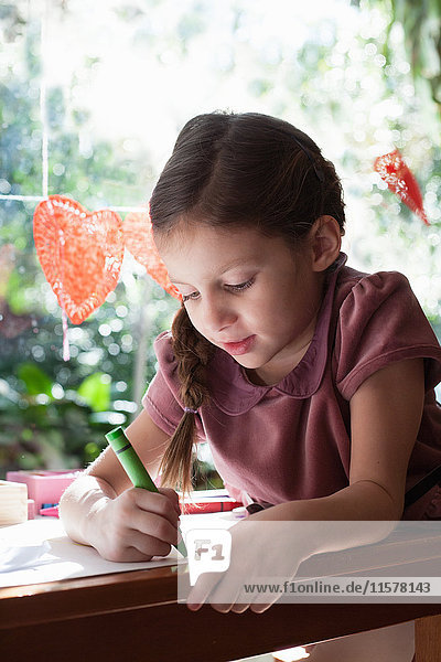 Mädchen sitzt am Fenstertisch und zeichnet mit Buntstift