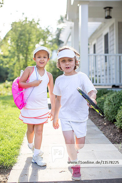 Portrait of boy and girl tennis players on garden path