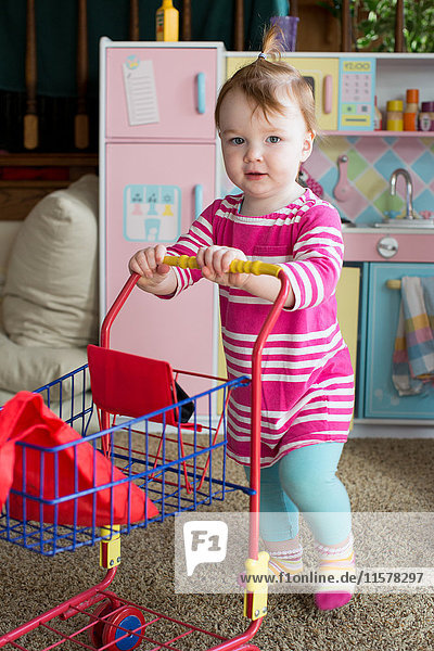 Porträt eines jungen Mädchens beim Schieben eines Spielzeug-Supermarktwagens