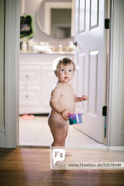 Portrait of naked female toddler standing in doorway