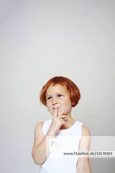 Porträt eines rothaarigen Mädchens im Haus  das seinen Finger vor den Mund hält  mit einem fragenden Gesichtsausdruck.
