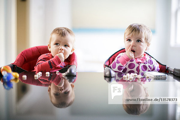 Male and female toddlers at kitchen counter picking nose and eating sweets