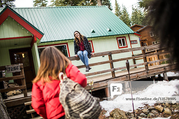 Mädchen sitzt auf dem Zaun der Hütte  ihre Freundin geht auf sie zu.