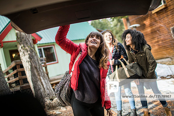Friends standing outside cabin  young woman closing boot of car