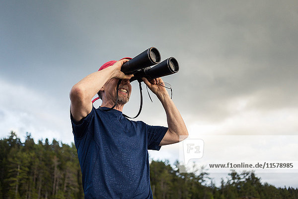 Senior man looking through binoculars toward coast of Maine  USA