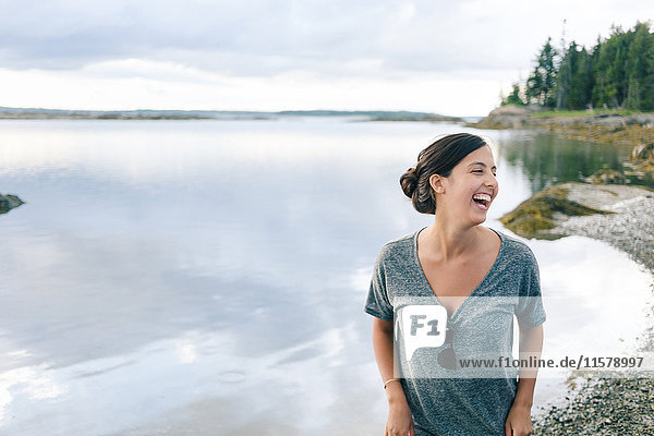 Young woman laughing on shingle beach  Maine  USA