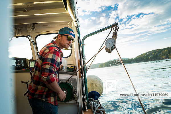 Young man raising winch on fishing boat on coast of Maine  USA