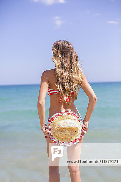 Hübsche blonde Frau im Bikini  die ihren Hintern am Strand versteckt und auf den Horizont schaut.