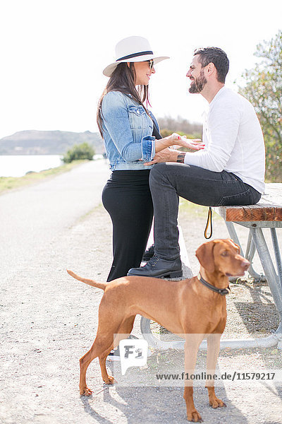 Ein schwangeres  reifes Paar diskutiert auf einer Parkbank an der Küste