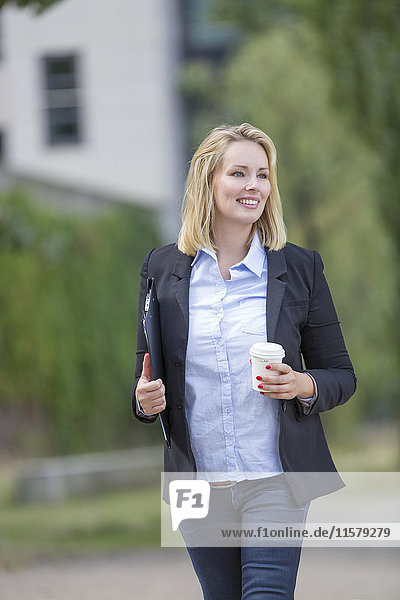 Hübsche Geschäftsfrau  die mit Kaffee im Freien spazieren geht.