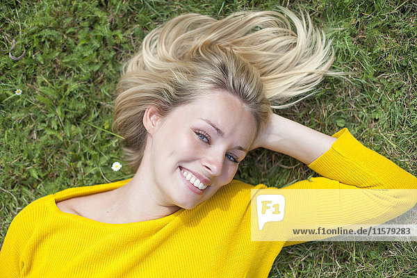 Porträt einer hübschen blonden Frau,  die im Park liegt und vor der Kamera lächelt.